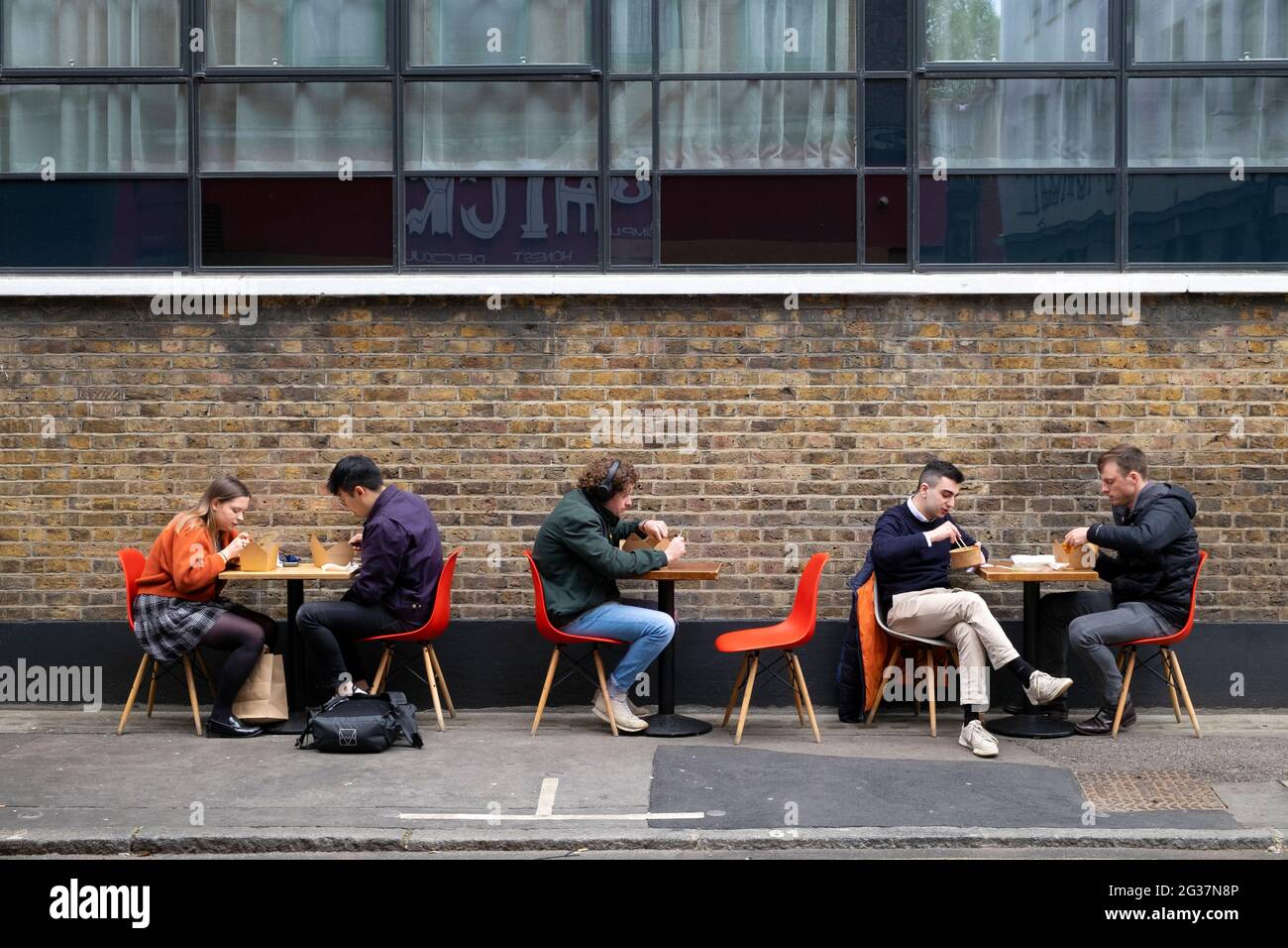 Persone che siedono a mangiare ai tavoli social distancing a pranzo in Leather Lane Street Market Londra Inghilterra UK 2021 KATHY DEWITT Foto Stock