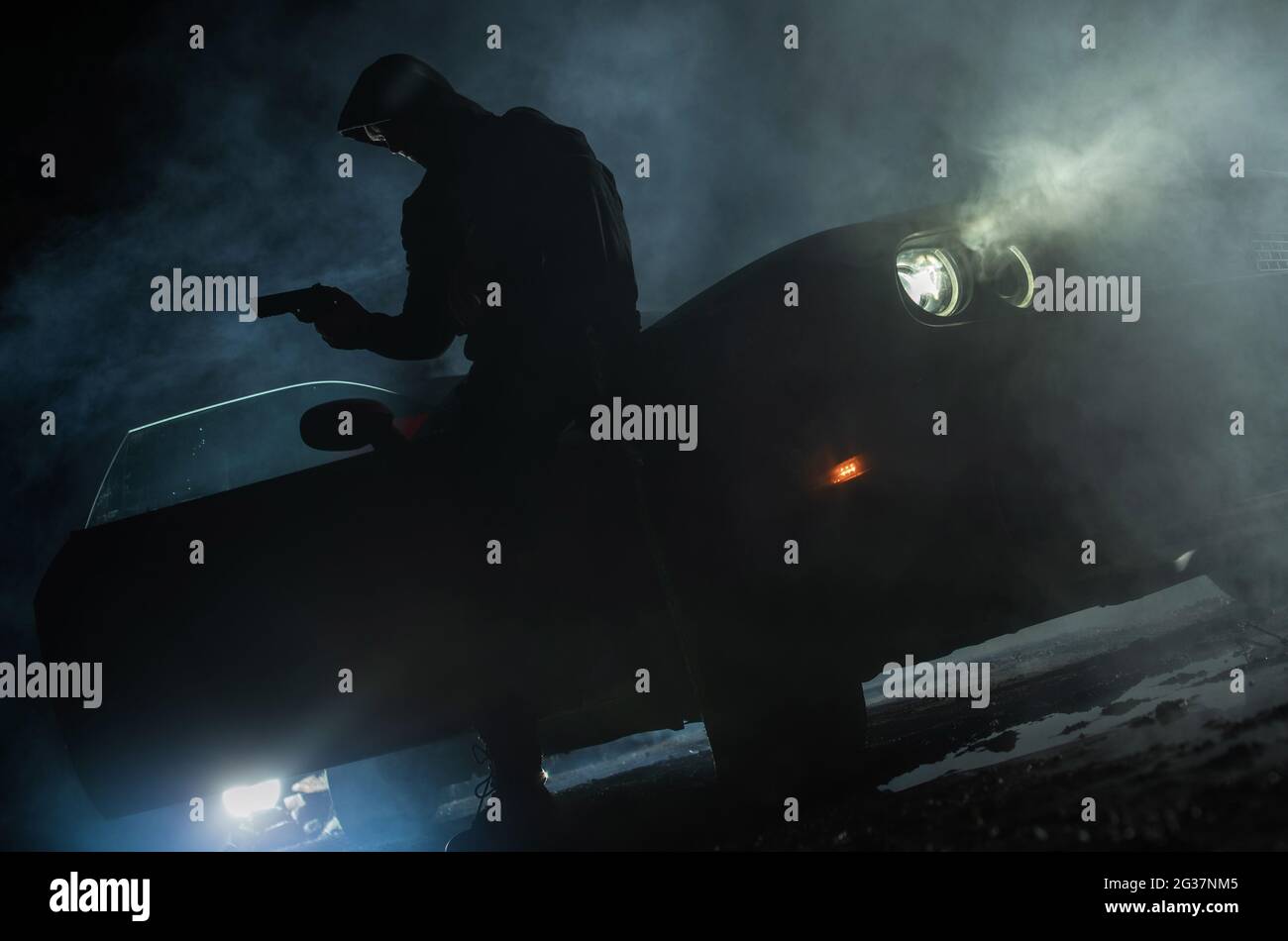Caucasico Drug Dealer indossare felpa con armi da fuoco in mano in attesa di qualcuno accanto alla sua auto. Scena notturna. Foto Stock
