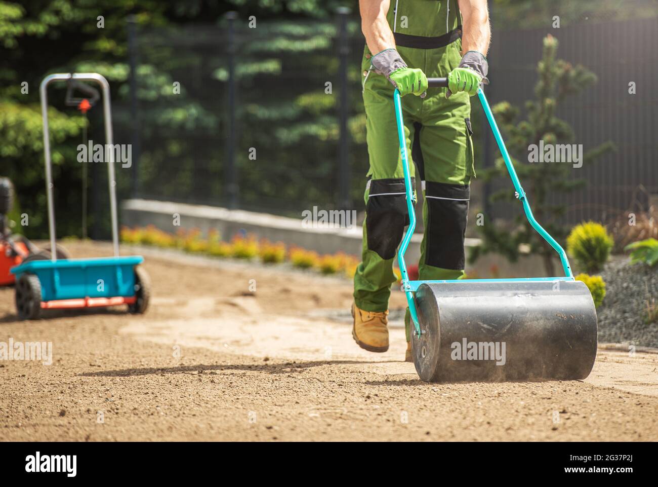 Poly Push Tow Lawn Roller spinto dal giardiniere caucasico. Compattazione del terreno prima della semina da erba. Preparazione del paesaggio del giardino. Giardinaggio e giardinaggio Th Foto Stock