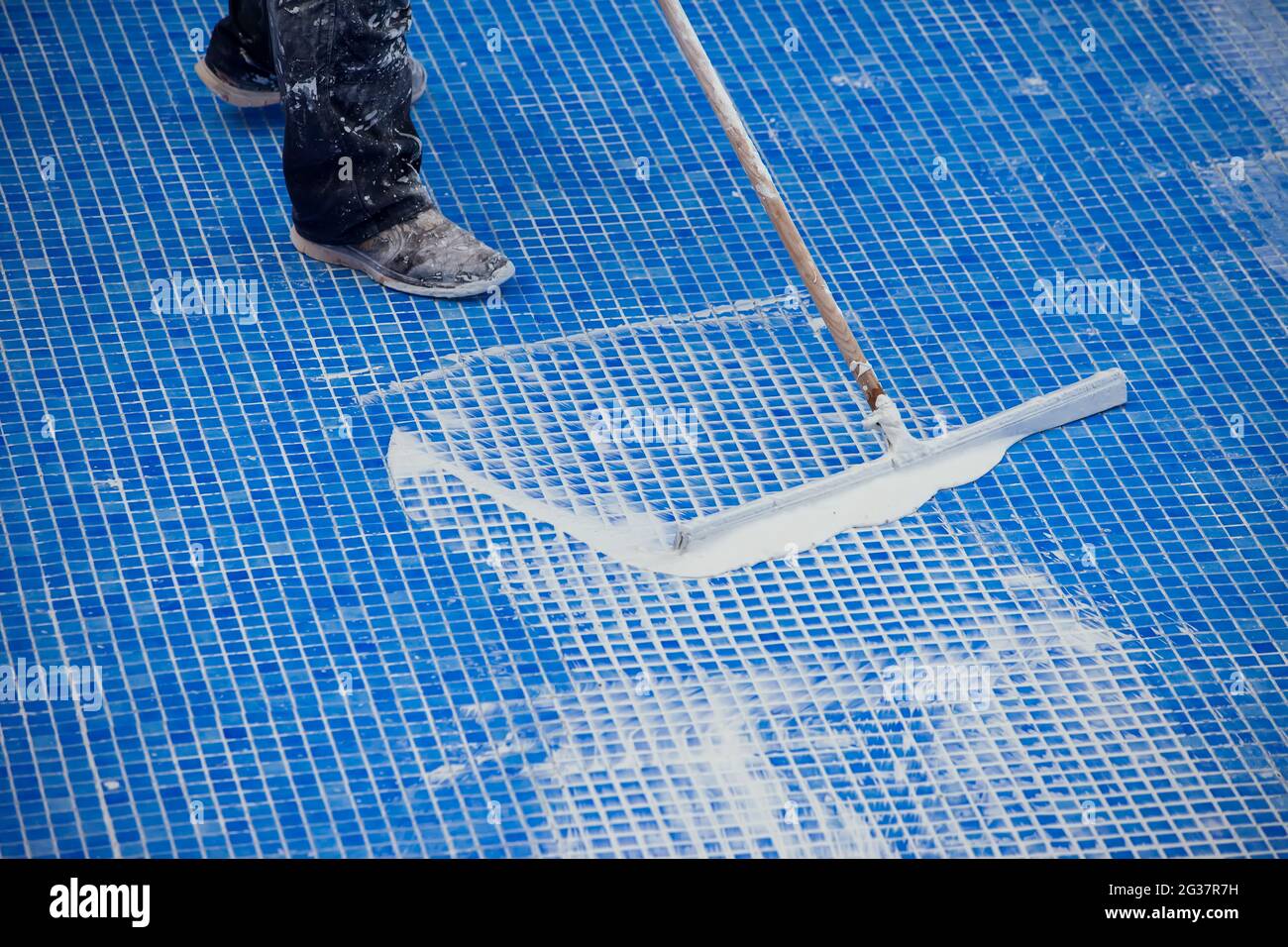 Lavoratore che copre le fiamme sulla piastrella in piscina. Lavori di riparazione della piscina Foto Stock