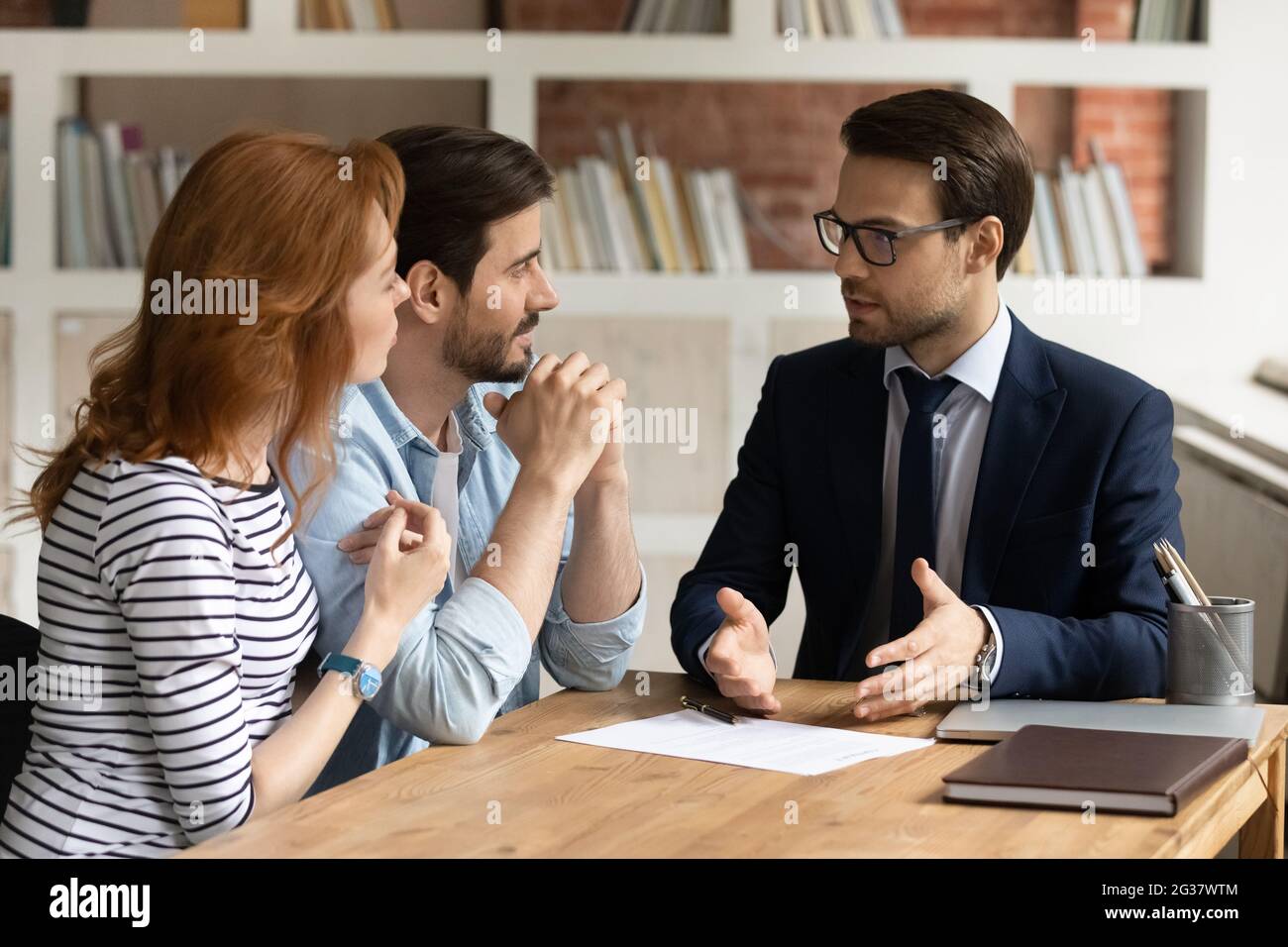 Giovane coppia di famiglia interessata che visita consulente finanziario in ufficio. Foto Stock