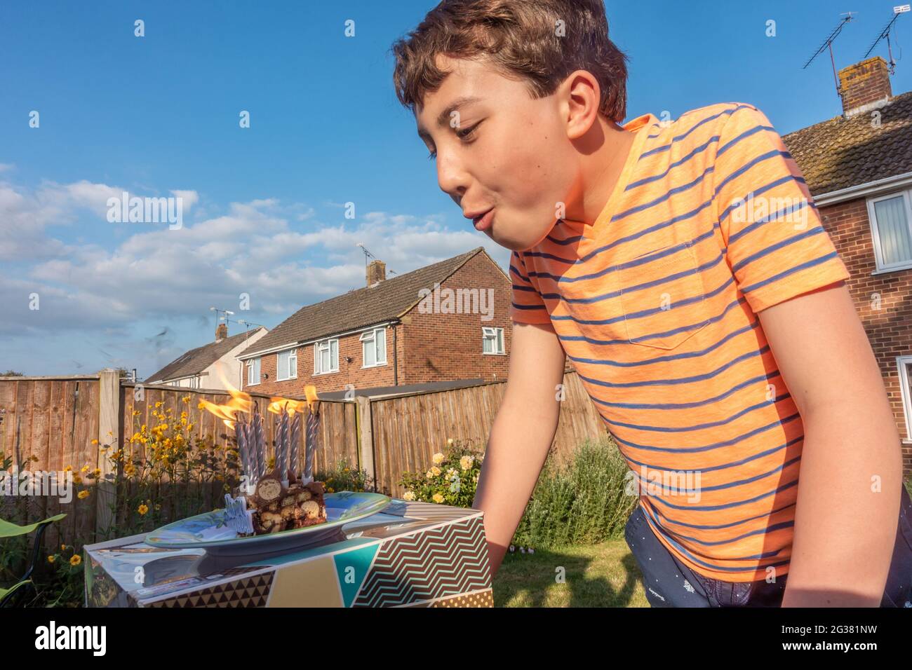 Un ragazzo soffia le candele su una fetta di torta di compleanno all'esterno in giardino, Foto Stock