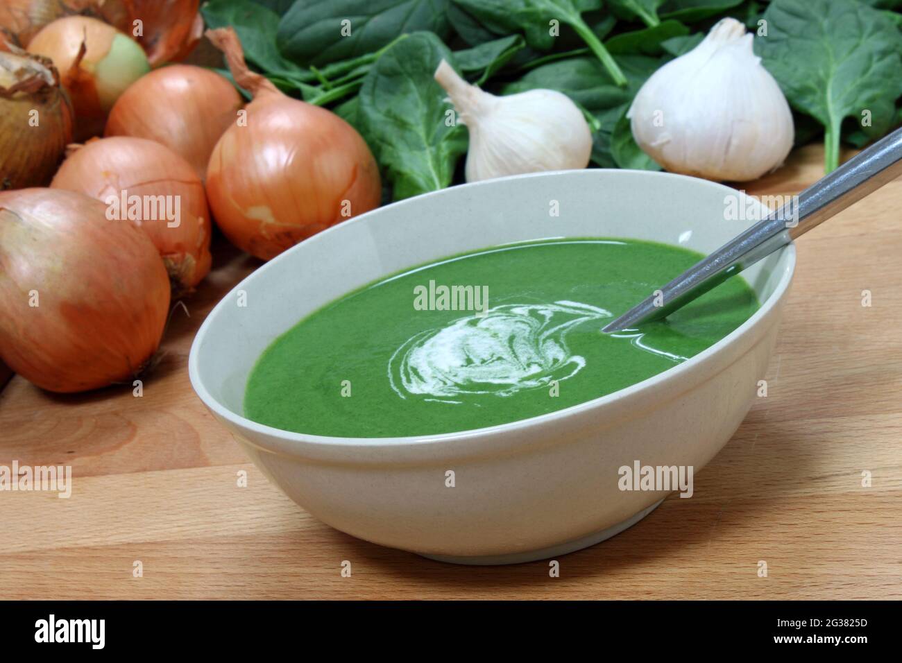 Una ciotola nutriente di zuppa di spinaci freschi, con alcuni degli ingredienti dietro. Foto Stock