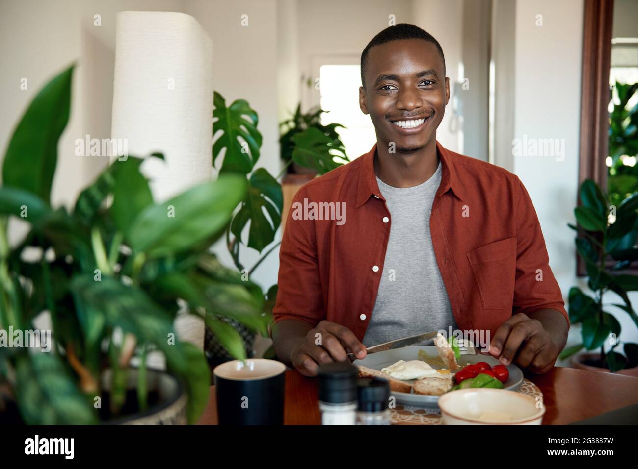 Sorridente giovane africano che mangia la colazione al suo tavolo da pranzo Foto Stock