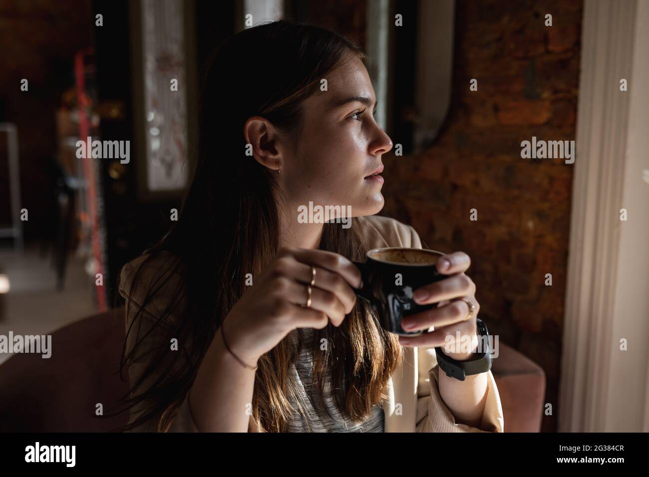 Donna caucasica seduta al tavolo, guardando la finestra esterna, bere caffè Foto Stock