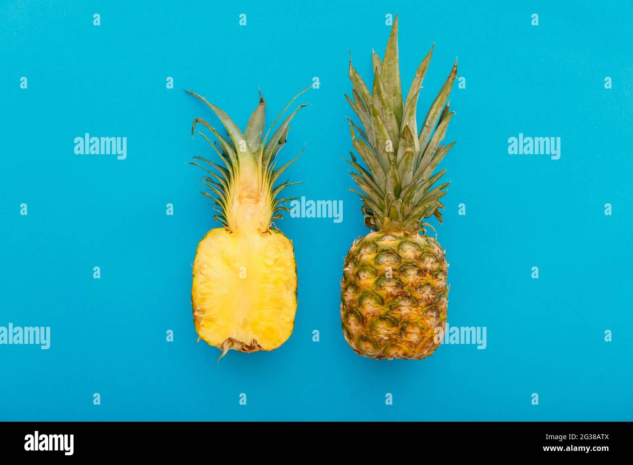 Frutta di ananas su sfondo estivo blu. Un intero ananas tropicale e mezzo frutto in stile minimalista su sfondo estivo di blu luminoso. Disposizione piatta Foto Stock