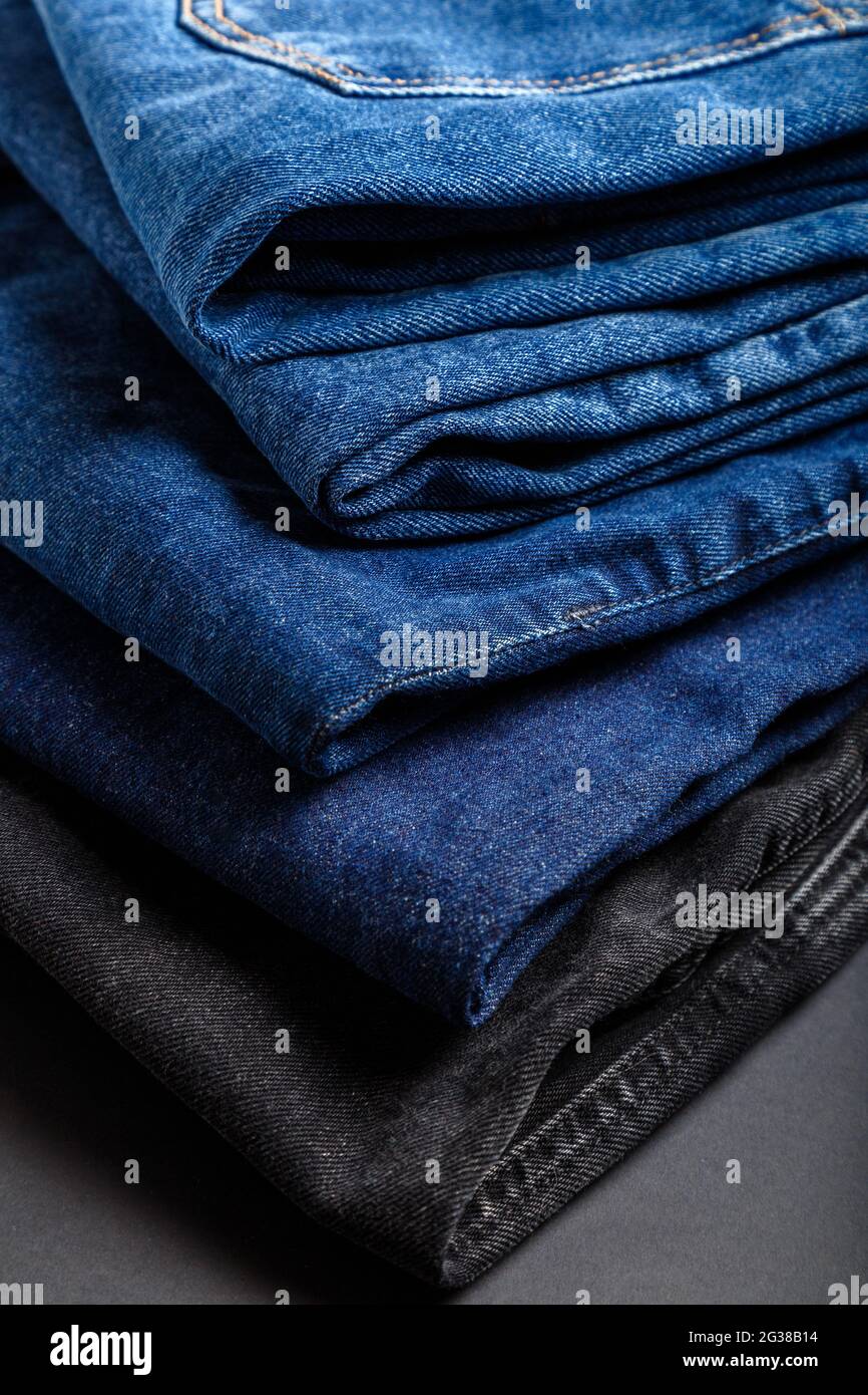 Pantaloni blu jeans stack tessuto tessuto tessuto sfondo. Stack di jeans blu varietà, tessuti denim jean su sfondo nero. Foto Stock