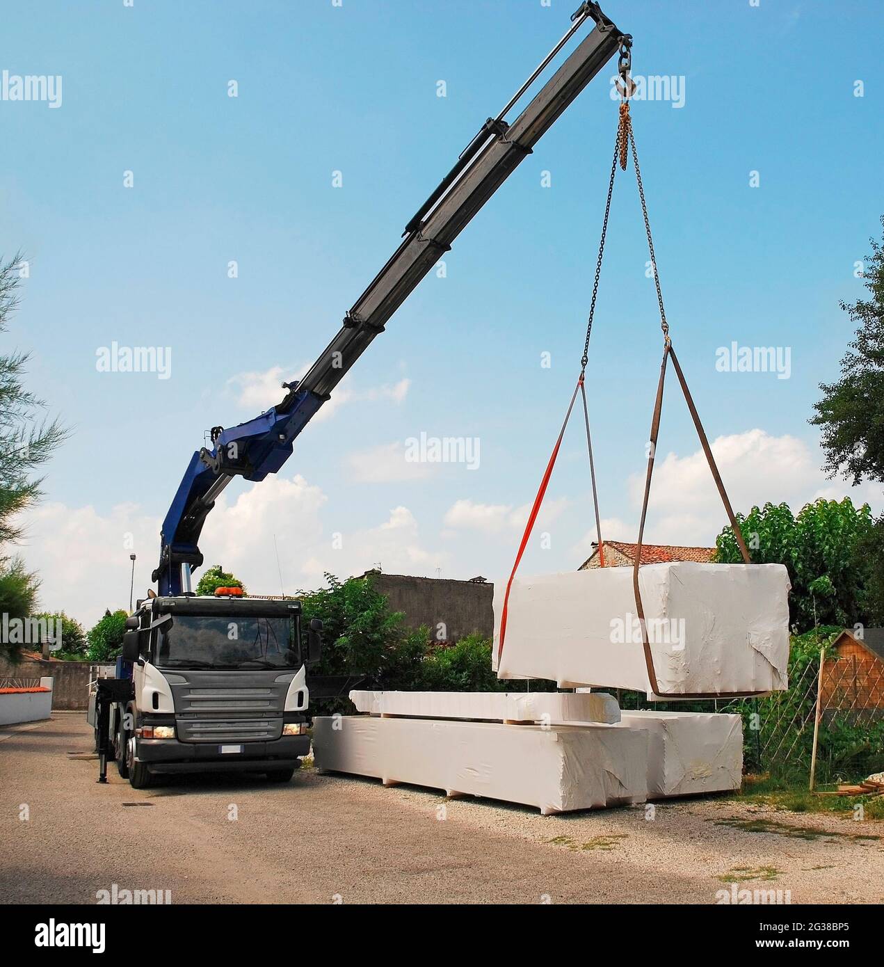 Un camion con gru telescopica consegna pacchi contenenti un blocco di legno (abete), una casa di legno pretagliata che viene montata sul posto. Udine Provin Foto Stock