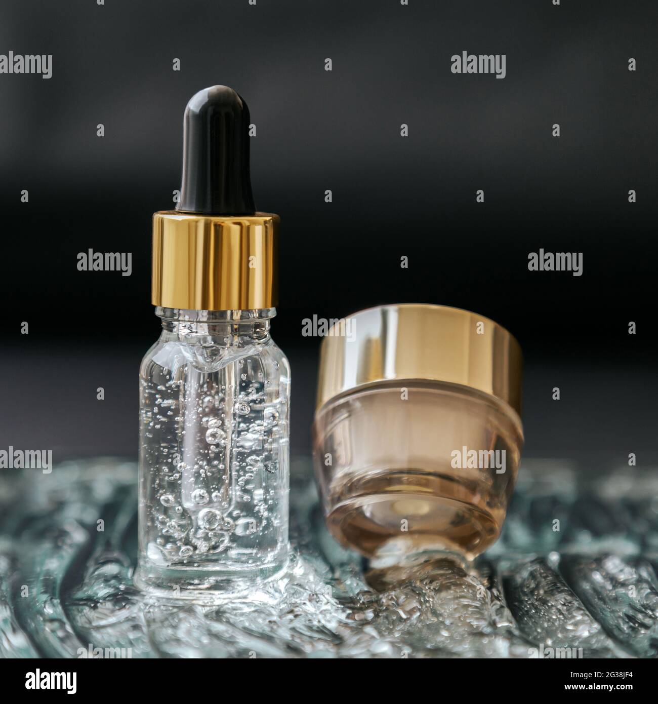 Skincare cosmetic Serum flacone con fluido collagene acido ialuronico, crema idratante vaso su acqua gel bolle superficie texture. Acqua d'oro di lusso Foto Stock