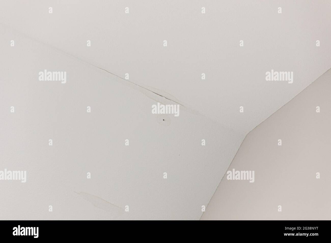 una piccola perdita d'acqua dal tetto su un soffitto bianco interno Foto Stock