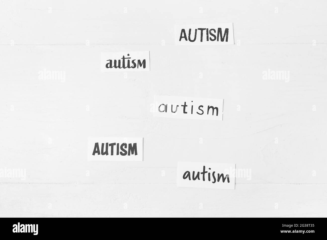 Pezzi di carta con parole AUTISMO su sfondo bianco di legno Foto Stock