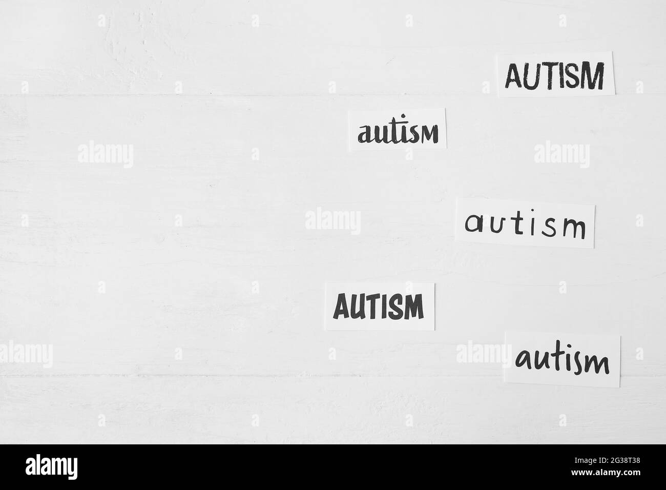 Pezzi di carta con parole AUTISMO su sfondo bianco di legno Foto Stock