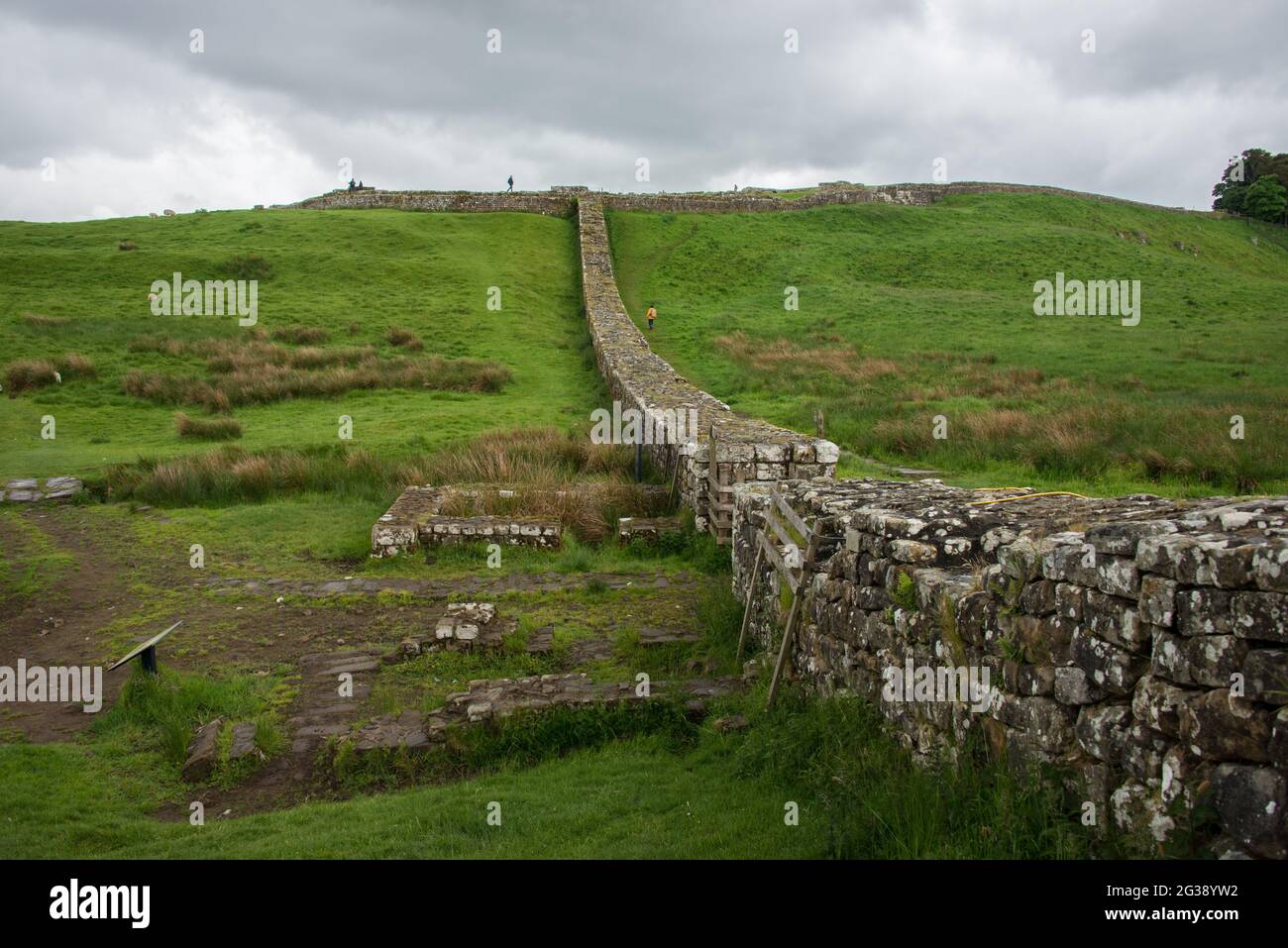 Segmento del Vallo di Adriano, l'antico muro di confine romano attraverso l'Inghilterra settentrionale, che corre in linea diretta fino al forte romano Housesteads sulla collina. In primo piano le mura della porta di Knag Burn, un vecchio percorso commerciale. Percorrendo tutto il sito patrimonio dell'umanità dell'UNESCO, il sentiero del Vallo di Adriano è uno dei percorsi escursionistici più popolari in Inghilterra. Foto Stock
