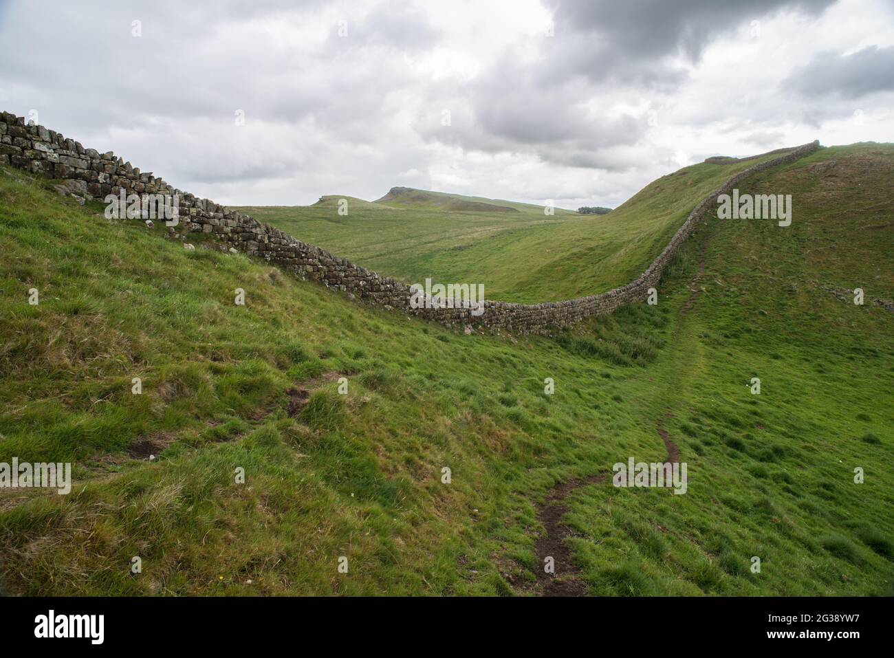 Resti di un segmento del Vallo di Adriano, l'antico muro di confine romano attraverso l'Inghilterra settentrionale, in costante salita e discesa seguendo la linea collinare a est del forte romano di Housesteads. Percorrendo tutto il sito patrimonio dell'umanità dell'UNESCO, il sentiero del Vallo di Adriano è uno dei percorsi escursionistici più popolari in Inghilterra. Foto Stock