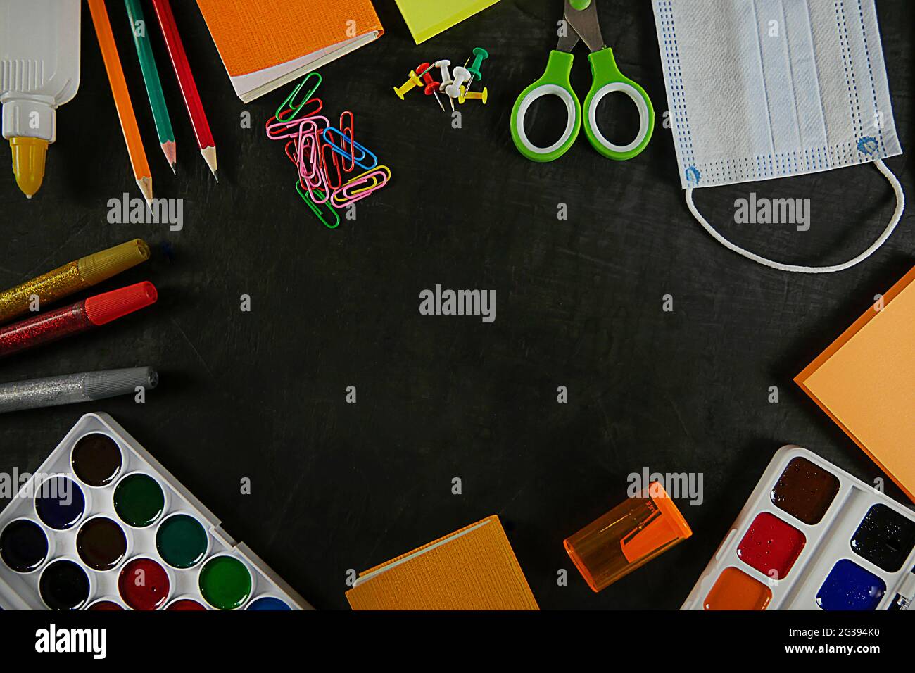 Ritorno a scuola, istruzione. Torna a scuola sulla lavagna nera della scuola. Matite di sfondo, vernici, visiera, graffette. Vista dall'alto. Copia Foto Stock