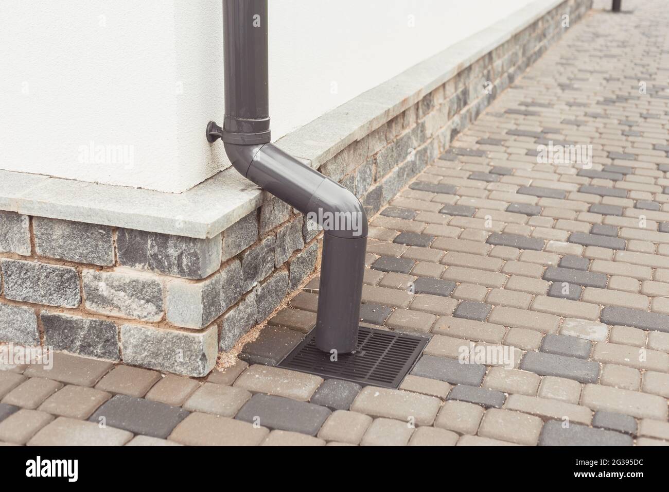 tubo di acqua piovana sulla facciata con scarico dell'acqua piovana nel sistema di drenaggio con griglia di tombino fognario Foto Stock