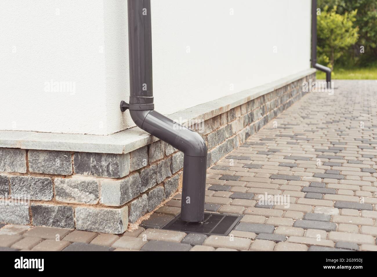 tubo di acqua piovana sulla facciata con scarico dell'acqua piovana nel sistema di drenaggio con griglia di tombino fognario Foto Stock