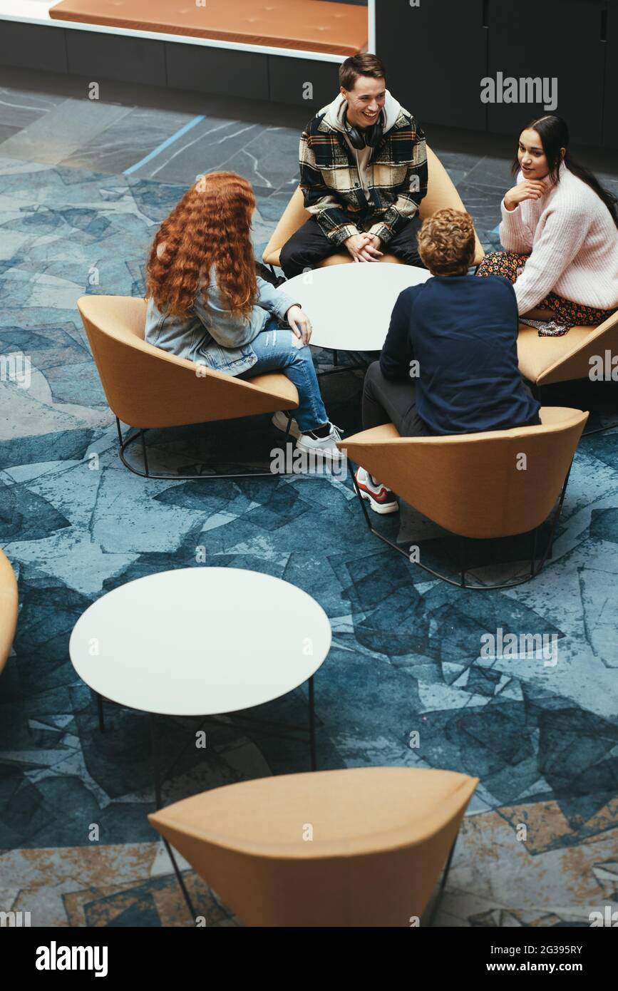 Gruppo di studenti che parlano e siedono intorno al tavolo nel campus universitario. Giovani nella hall del campus universitario. Foto Stock
