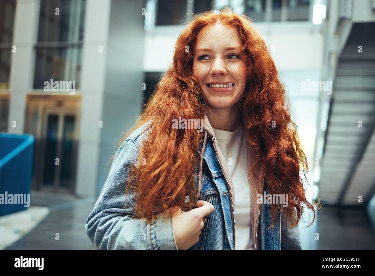 Giovane donna che va a classe in università. Ragazza in piedi nel campus universitario guardando via e sorridente. Foto Stock