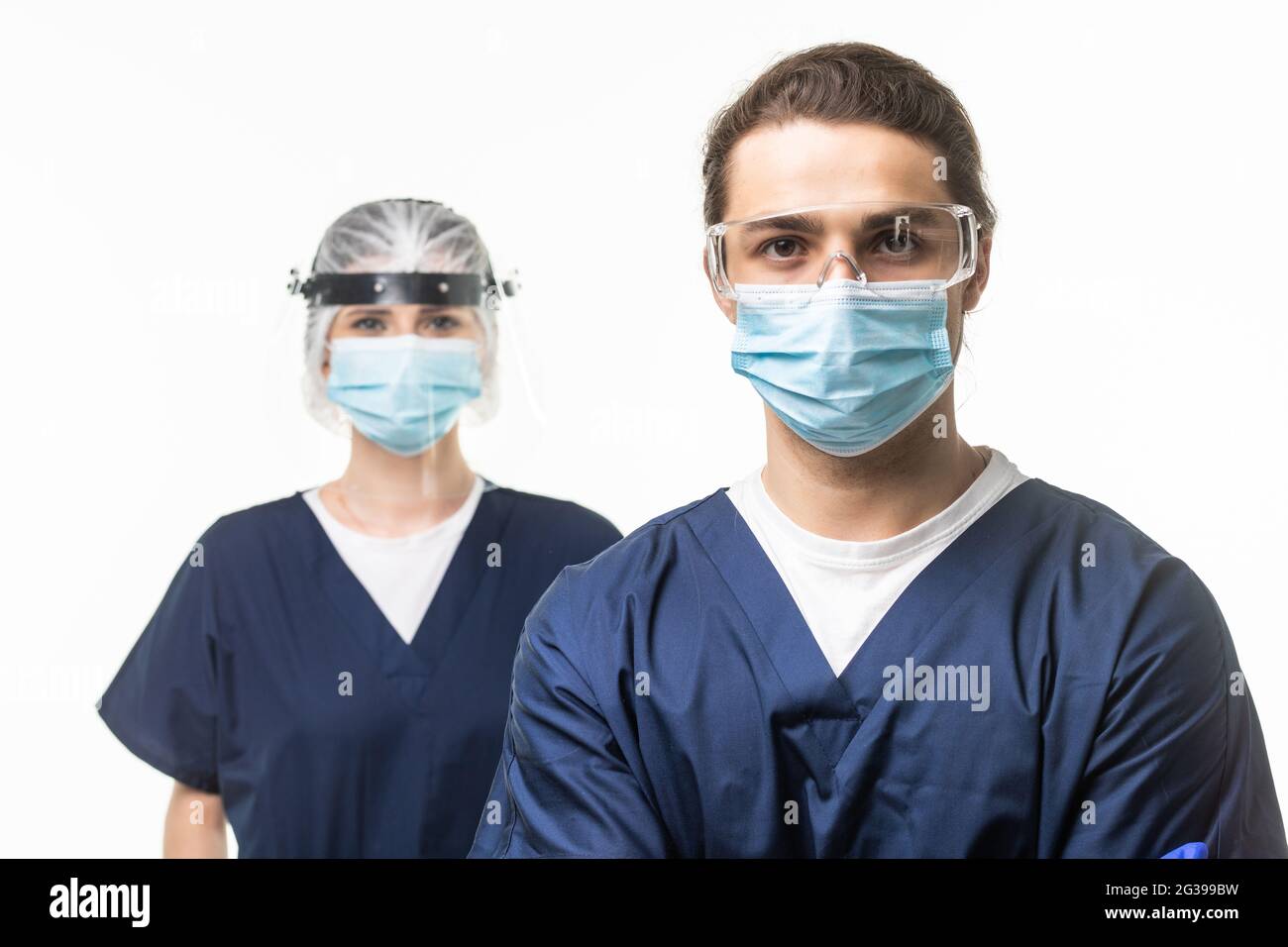 Due medici di entrambi i sessi in bianco camice da laboratorio e maschera protettiva si guarda l'uno sull'altro in piedi con le braccia piegate su sfondo bianco. Assistenza sanitaria, Foto Stock