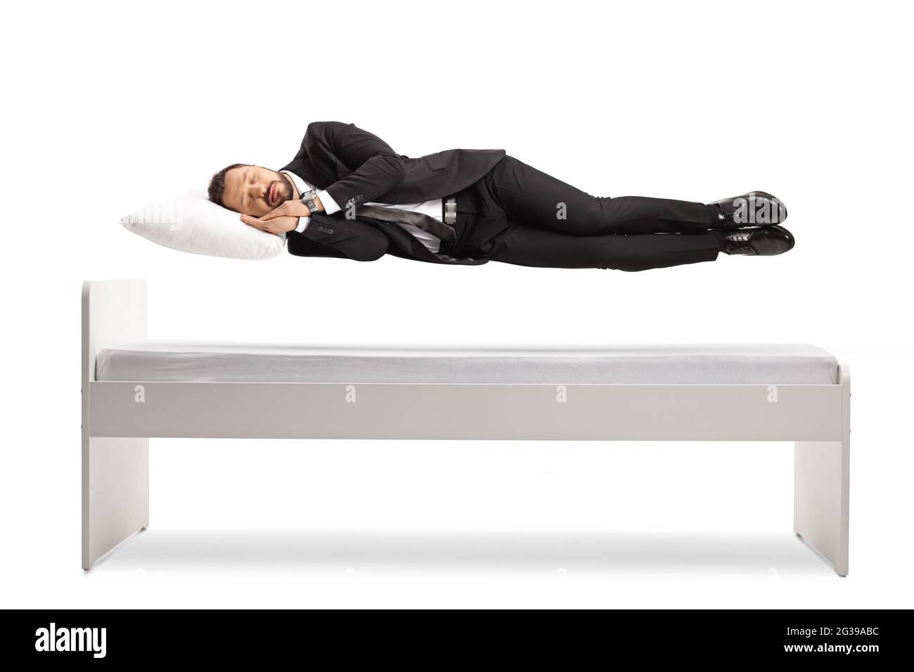 Uomo in tuta e cravatta dormendo e galleggiando sopra il suo letto isolato su sfondo bianco Foto Stock
