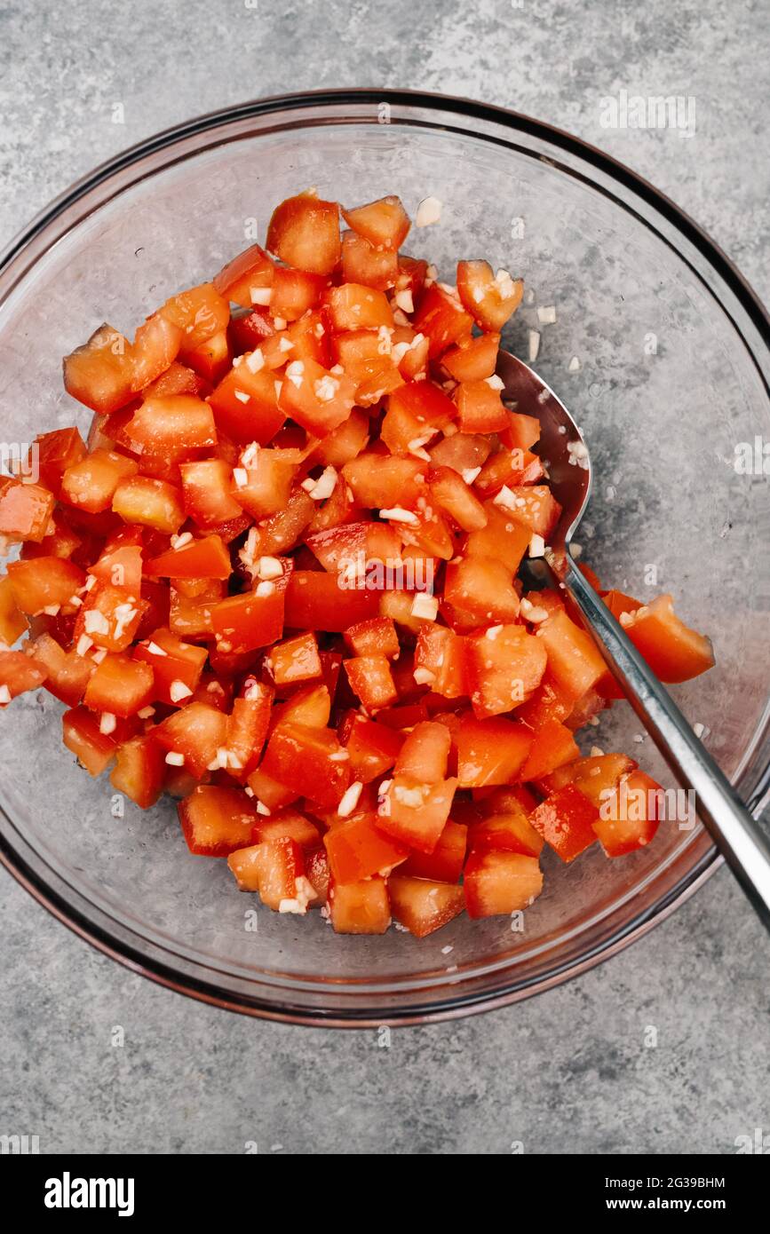 I pomodori e l'aglio tagliati a dadini in un recipiente di miscelazione in vetro Foto Stock