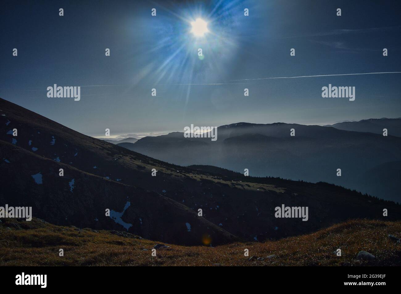 paesaggio montano e collinare in controluce con macchie di neve, erba e cielo blu Foto Stock