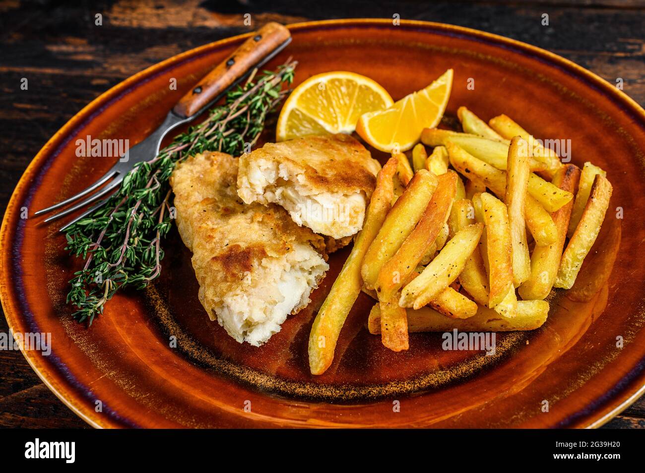 Pesce e patatine fritte inglesi con patatine fritte e salsa tartaro su un piatto rustico. Sfondo di legno scuro. Vista dall'alto Foto Stock