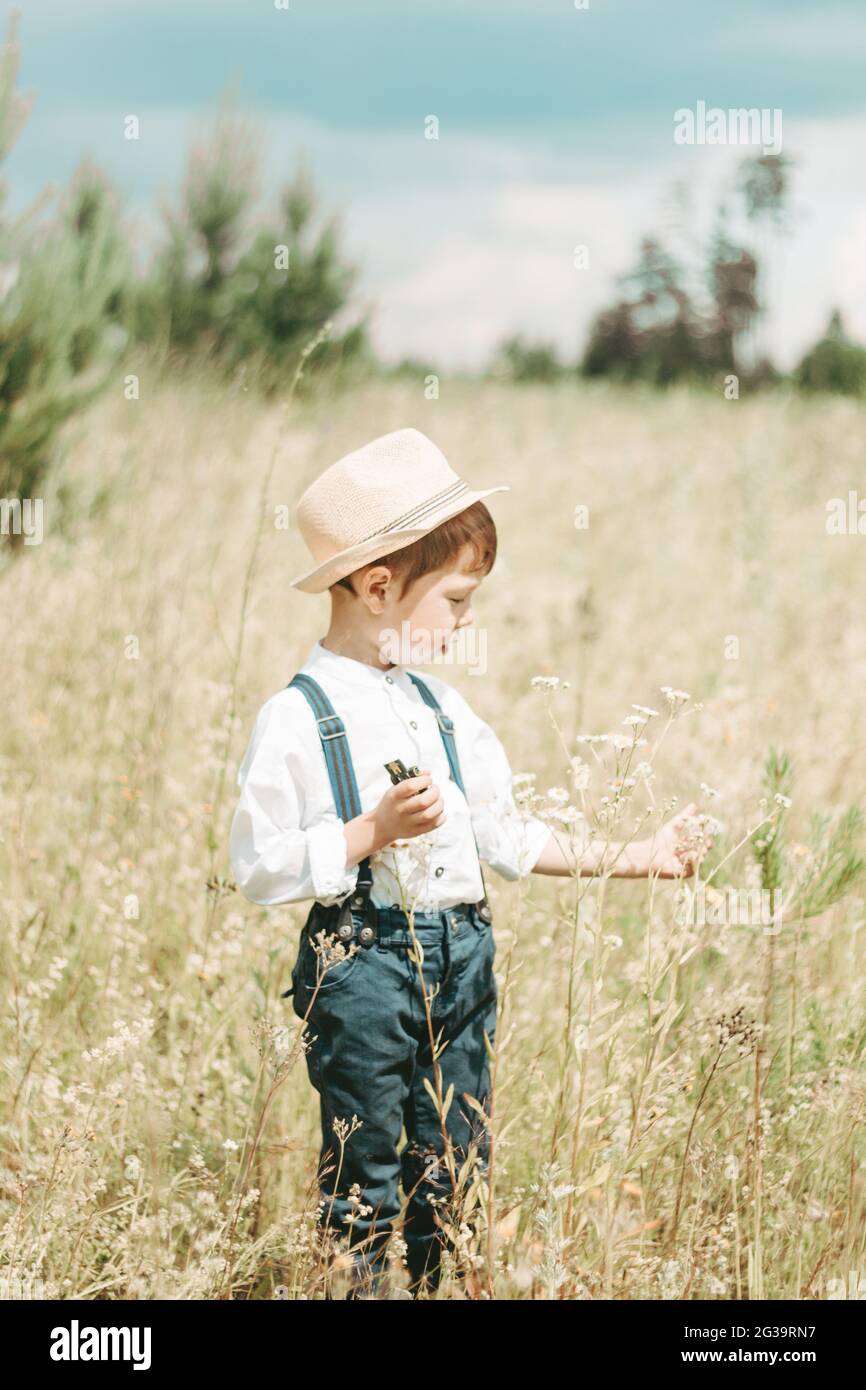 Piccolo contadino nel campo estivo, simpatico ragazzino in un cappello di  paglia. Ragazzo raccoglie fiori nel campo. Ragazzo in stivali di gomma e  una camicia bianca. Paese s Foto stock - Alamy