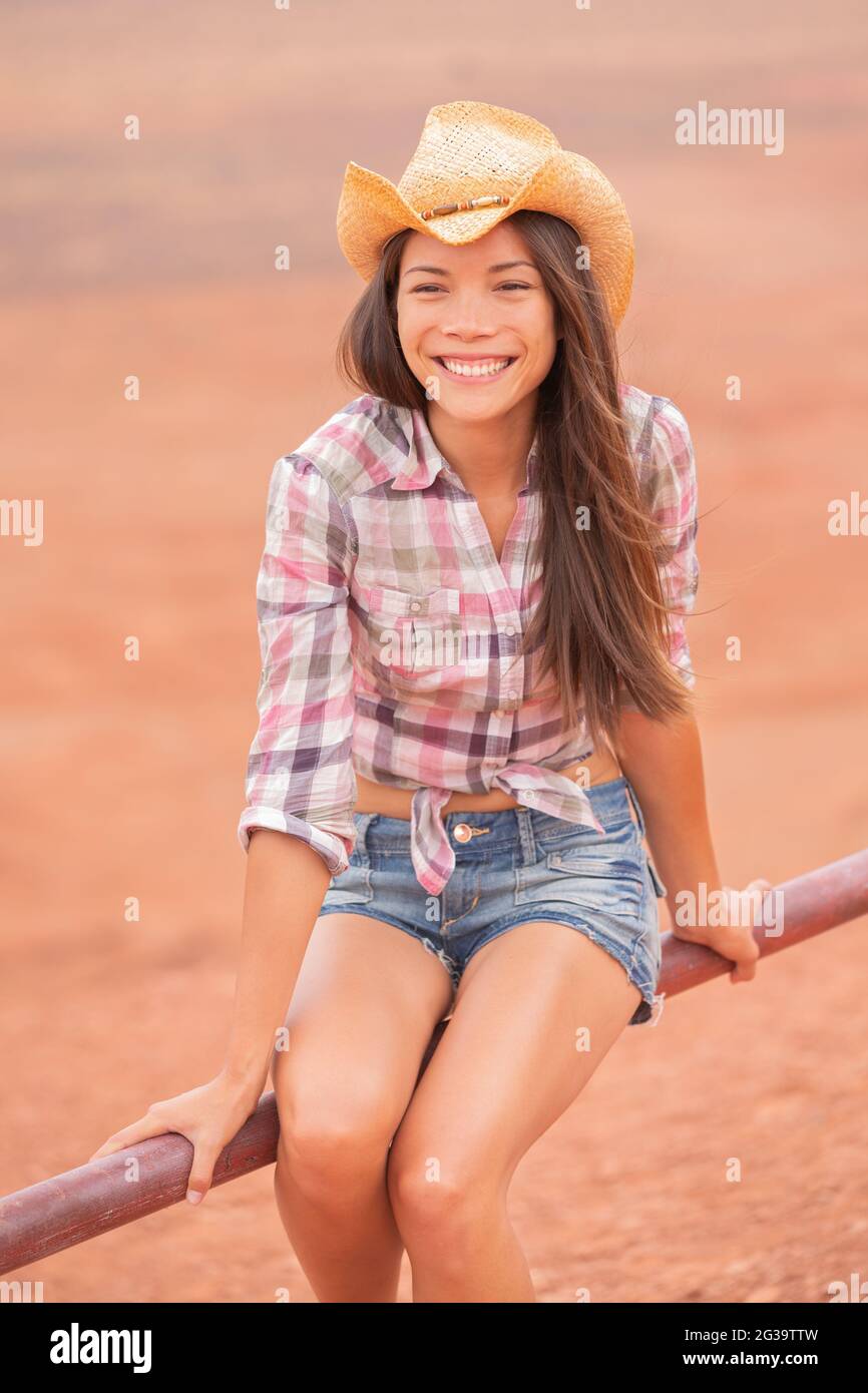 Cowgirl Texas donna sorridente felice sul ranch fattoria di campagna che  indossa cappello cowboy, camicia occidentale e jeans shorts. Giovane ranch  asiatico-americano multirazziale Foto stock - Alamy