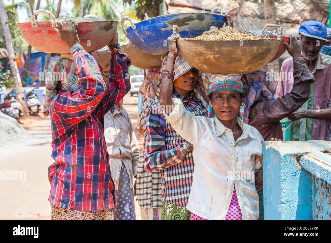 Lavoratrice manuale indiana femminile che trasporta il carico pesante sulla sua testa pone per la fotografia al luogo di costruzione, Agonda, Goa, India Foto Stock