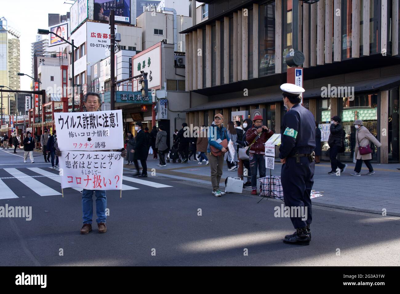 Maschio giapponese che detiene cospirazione Covid e poster vaccino anti covid-19 lungo via Kaminarimon-Dori, Asakua, Tokyo, Giappone Foto Stock