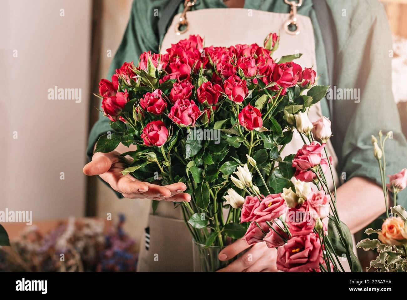 Fiorista donna sta tenendo un grande bouquet di rose. Ambiente di lavoro fiorista. Concetto di piccola impresa. Negozio di fiori e accessori. Primo piano Foto Stock