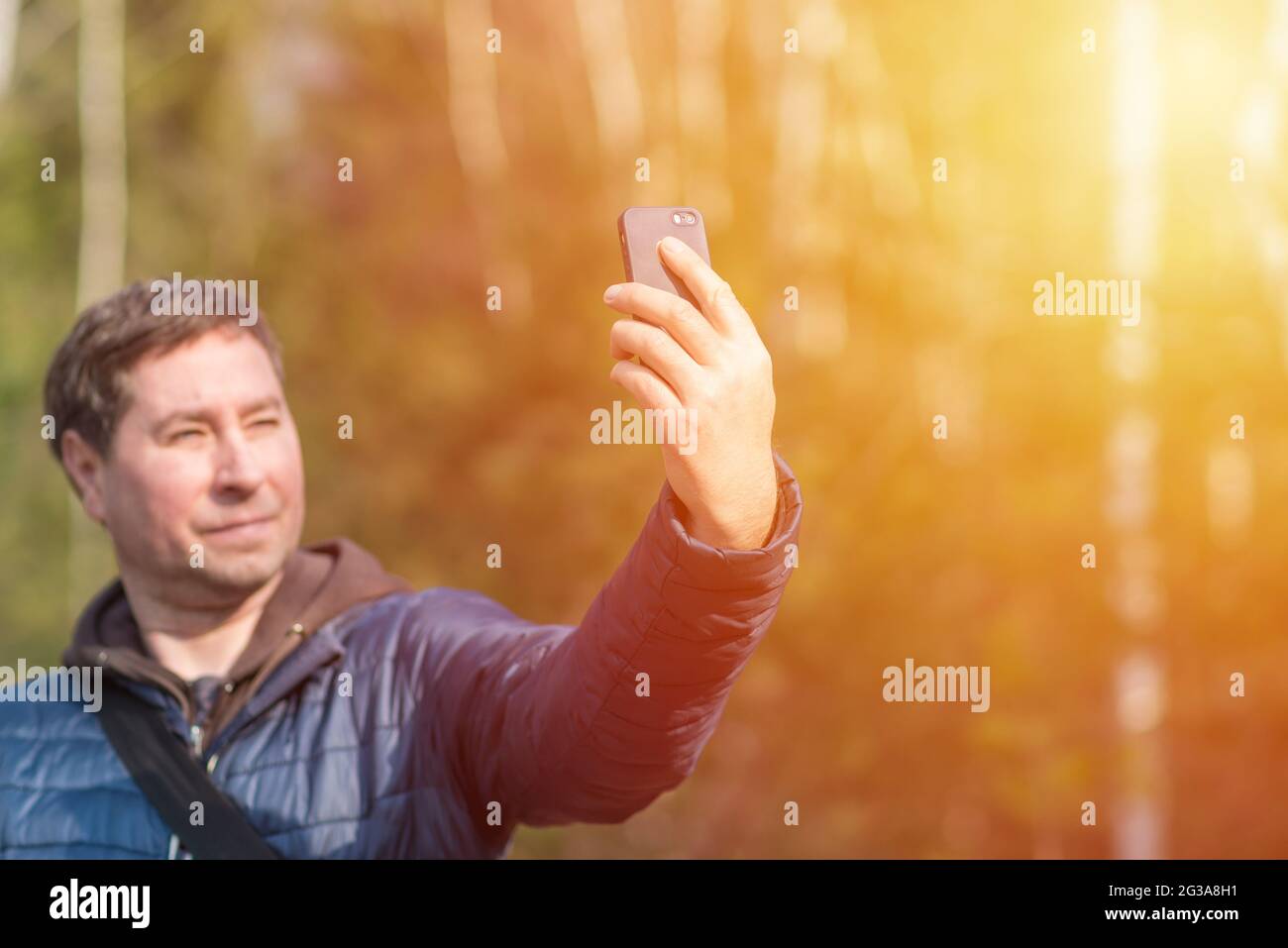 Un uomo di 40 anni con il suo smartphone cellulare alla ricerca del segnale di ricezione nella foresta primaverile soleggiata. Foto Stock