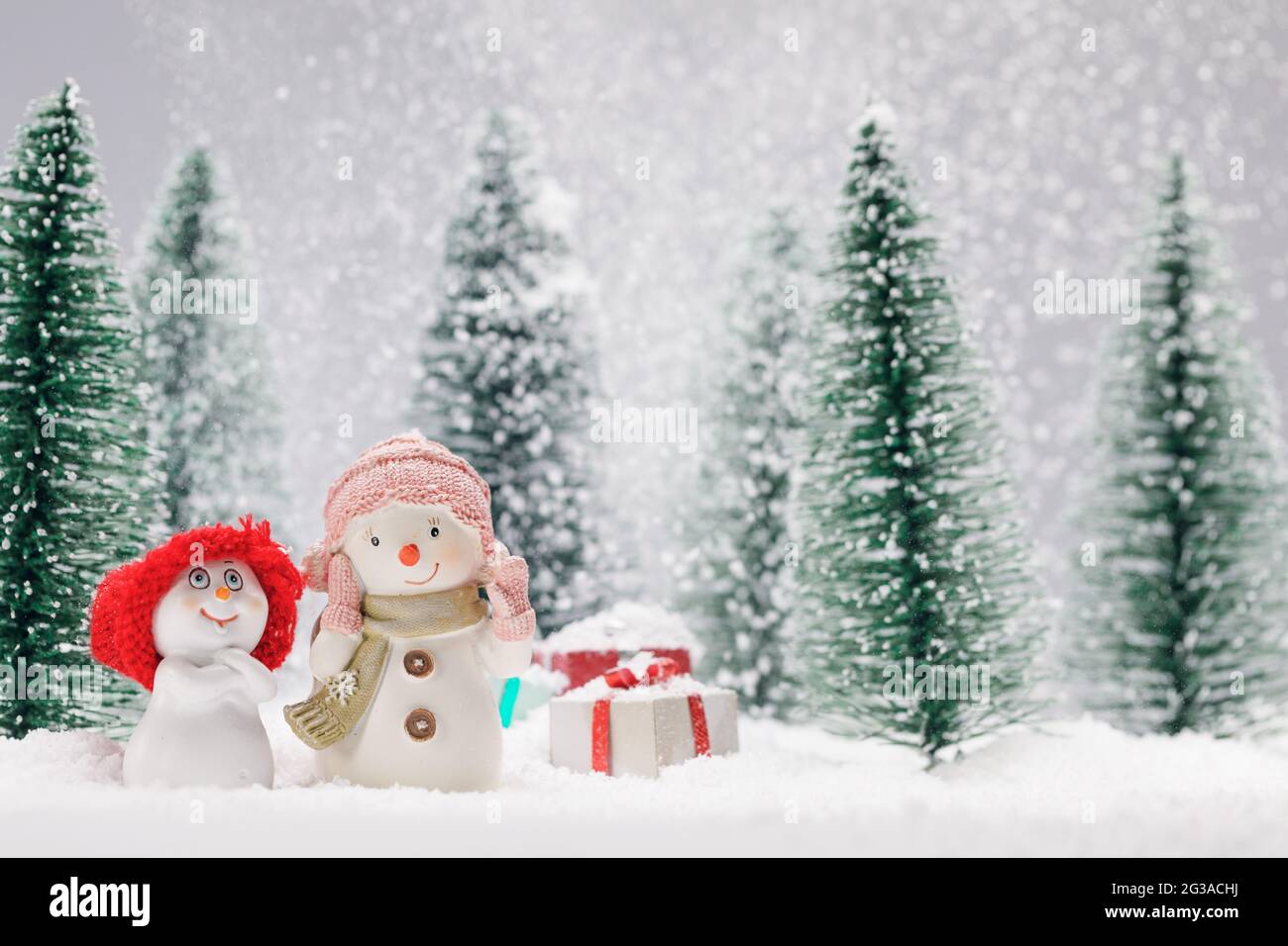 Due piccoli Simpatici pupazzi di neve amici con doni nella foresta sotto la caduta di neve Foto Stock