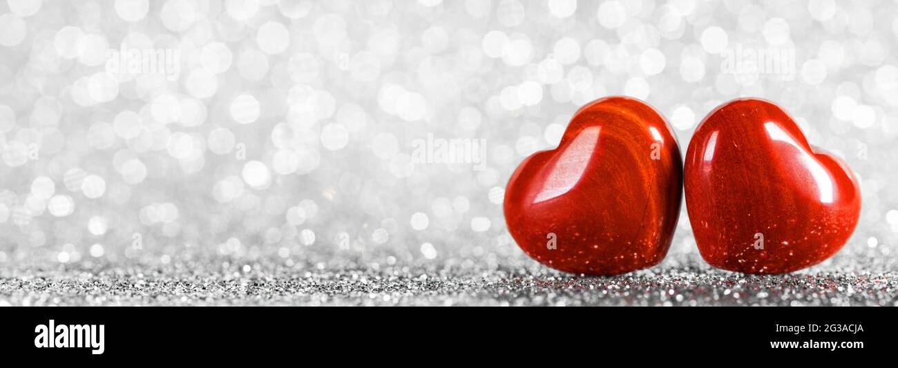 Due piccoli cuori di legno rosso fatti a mano su luci argentate brillanti bokeh sfondo carta giorno di San Valentino Foto Stock