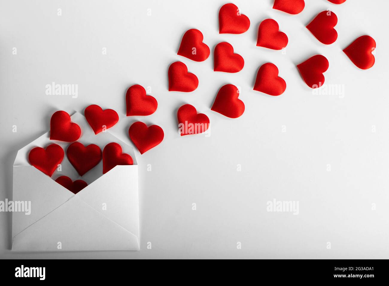 Lettera d'amore di giorno di San Valentino, busta di carta bianca con heap di cuori rossi sparsa su sfondo bianco. Foto Stock