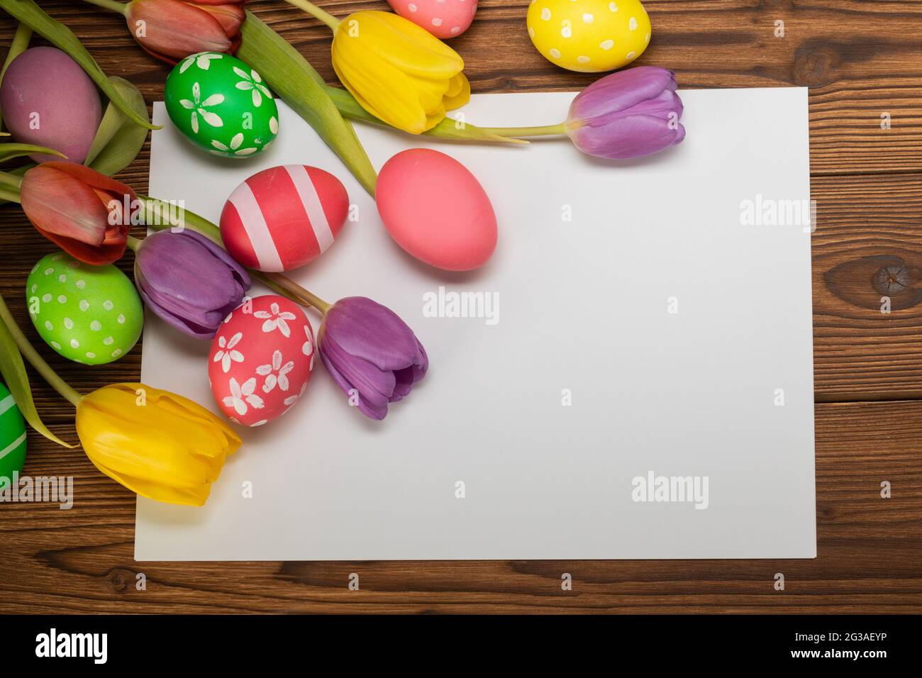 Uova di pasqua dipinte a mano con tulipani su sfondo di legno e spazio di copia di carta per testo top view template Foto Stock
