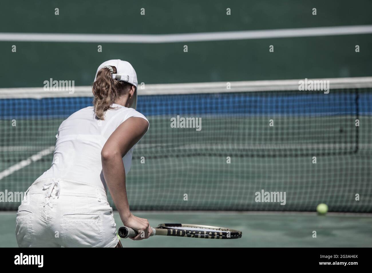 Vista posteriore di donna in uniforme da tennis bianca che gioca a tennis sul campo Foto Stock