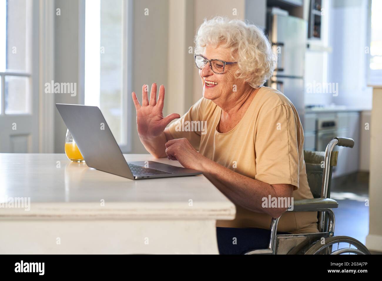 Donna anziana felice in sedia a rotelle che fa la videochiamata con la famiglia a casa e che agita Foto Stock