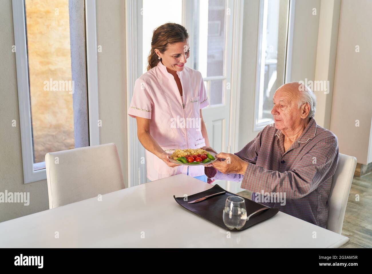 La moglie del servizio infermieristico o assistente di cura serve il pranzo per l'uomo anziano nel suo appartamento Foto Stock