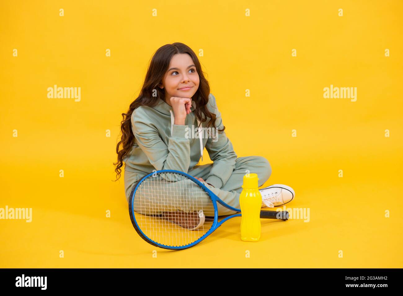 bambino sorridente seduto in abbigliamento sportivo con racchetta da squash e bottiglia d'acqua su sfondo giallo, sport Foto Stock