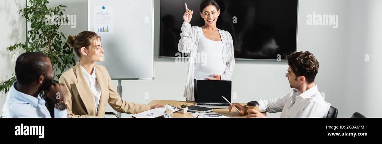 donna d'affari americana incinta che punta con il dito mentre parla con i soci d'affari, bandiera Foto Stock