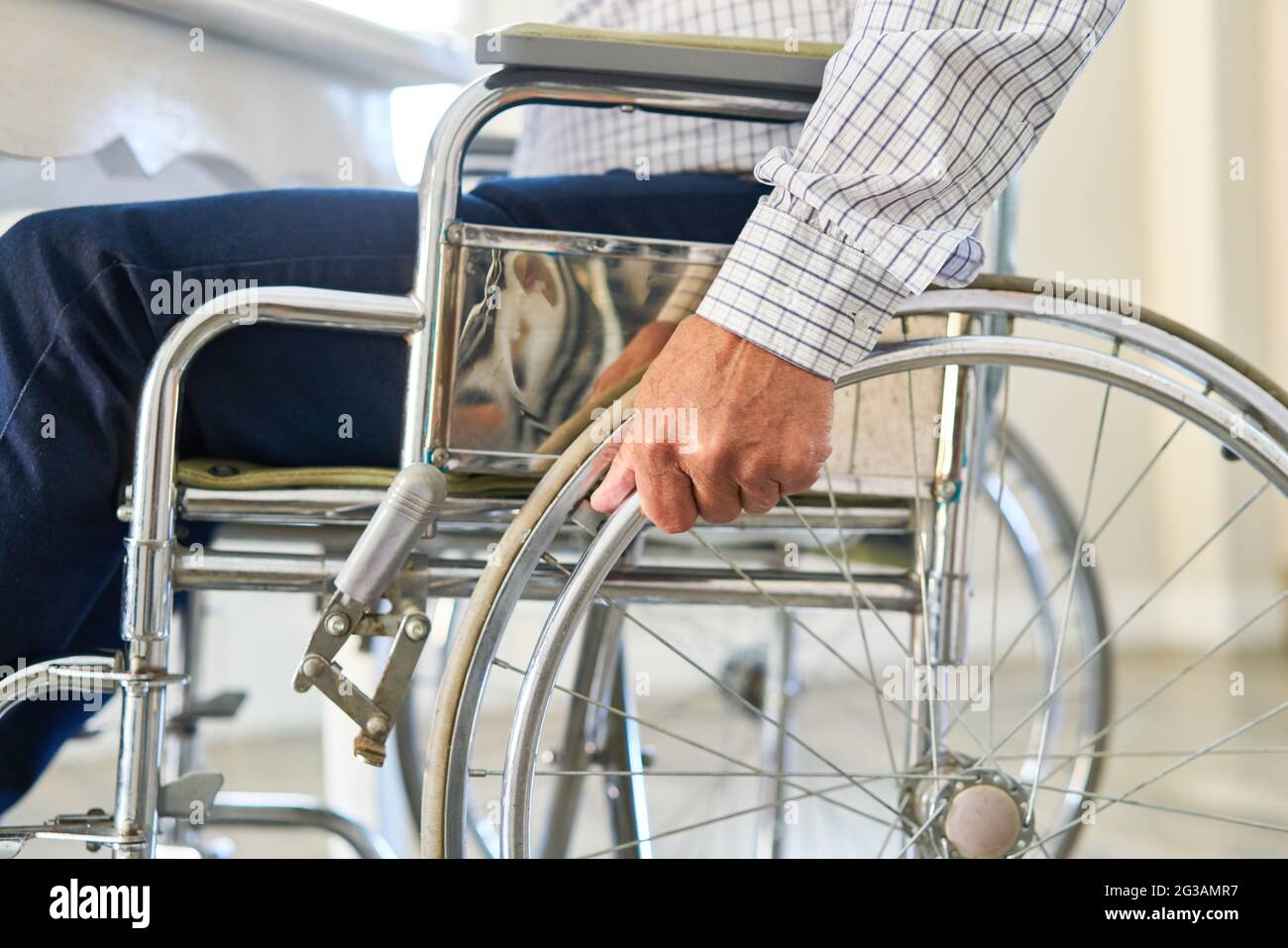 Mano di anziano dopo l'ictus sulla ruota di una sedia a rotelle come simbolo per disabilità e handicap Foto Stock