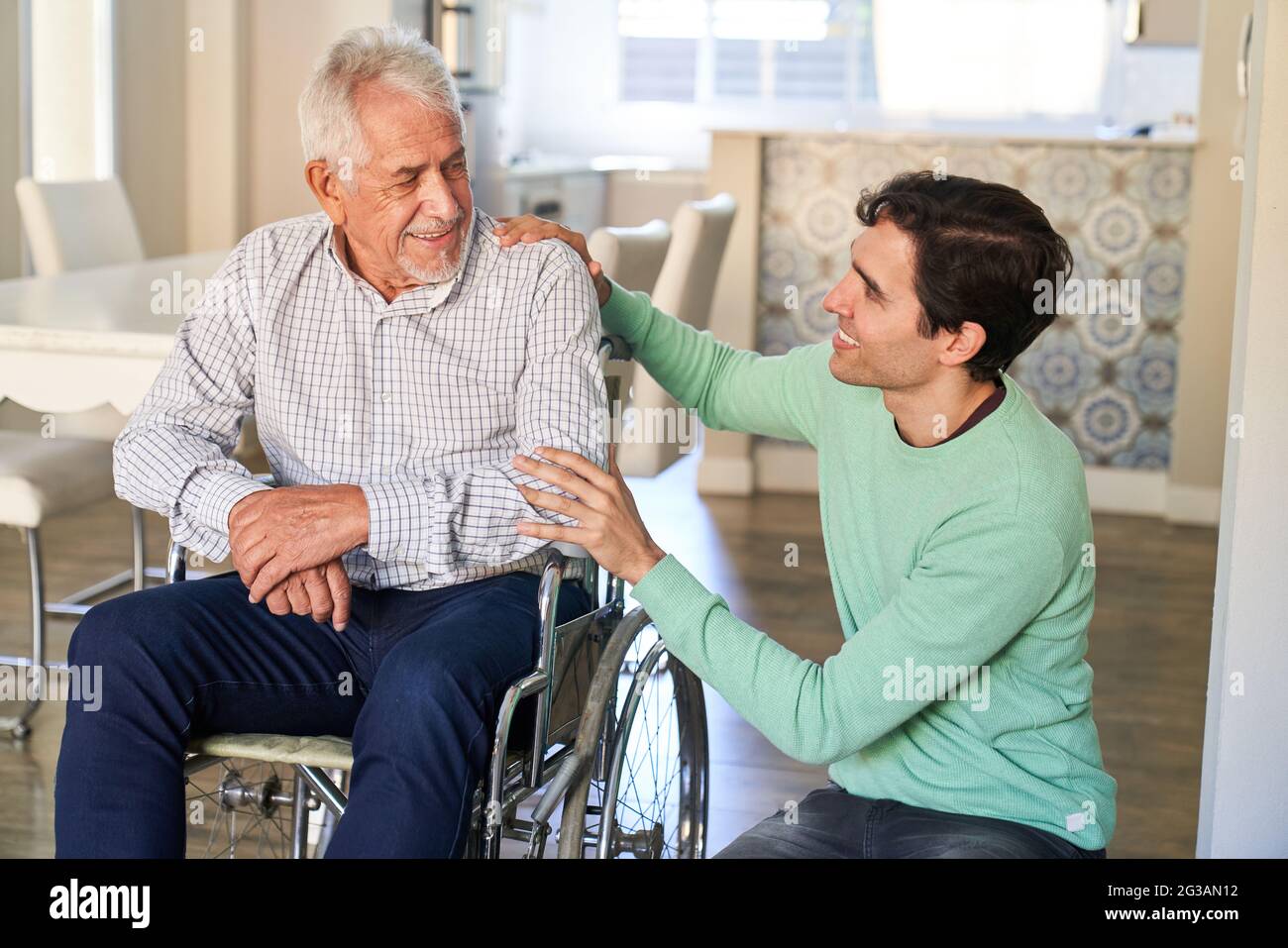 Uomo sorridente che si prende cura dell'uomo anziano in sedia a rotelle in progetto di vita assistita Foto Stock