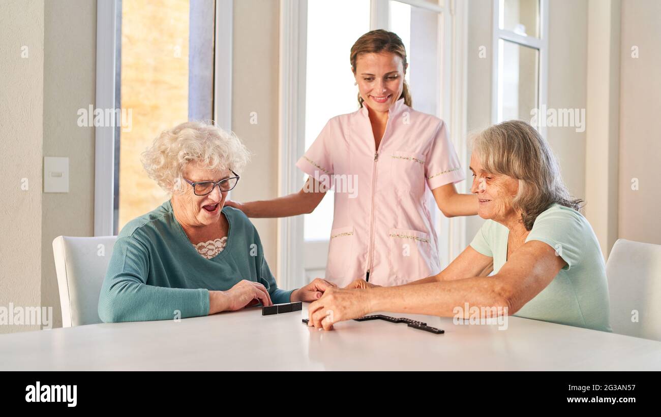 Due donne anziane che giocano a domino con cura da un caregiviere in una casa di cura Foto Stock