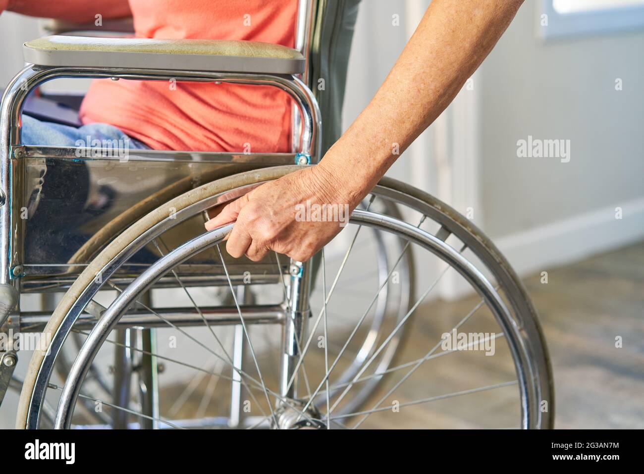 Mano di un paziente con un colpo sulla ruota di una sedia a rotelle come simbolo di handicap e disabilità Foto Stock