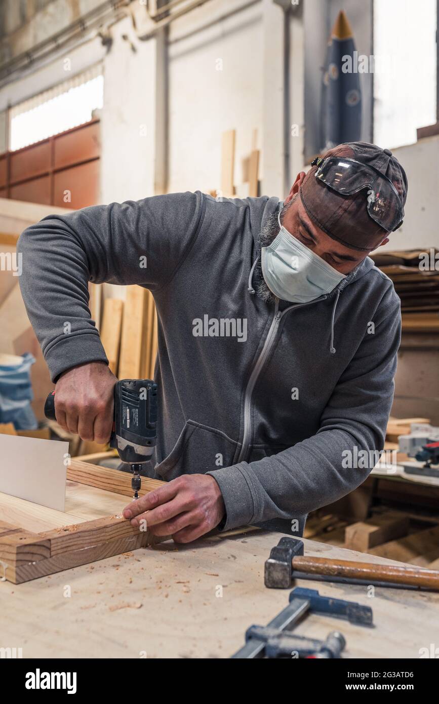 carpentiere con maschera avvitando una vite con un cacciavite elettrico Foto Stock