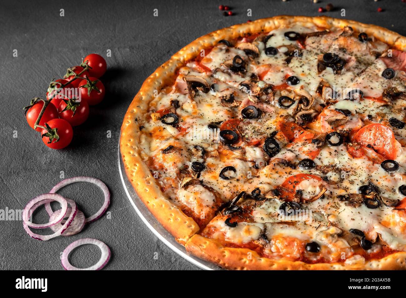 Pizza italiana con formaggio, olive, pomodoro, cipolla, salsiccia di peperoni su tavola grigia, primo piano Foto Stock