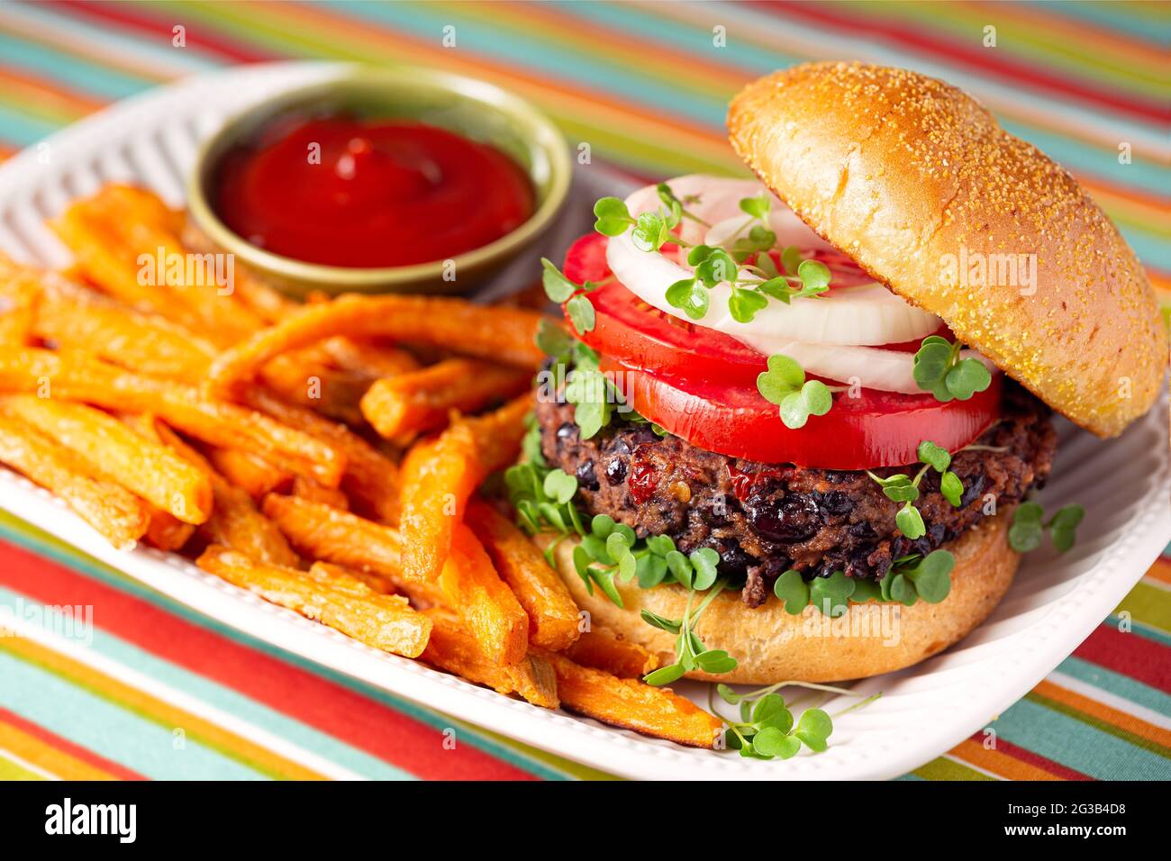 Hamburger di avocado di fagioli neri a base di piante con pomodoro, micro green e cipolla rossa serviti con patatine dolci e ketchup Foto Stock